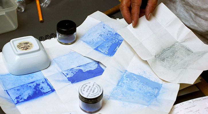 A collection of papers painted with different grades of ultramarine paint, and pots of paint