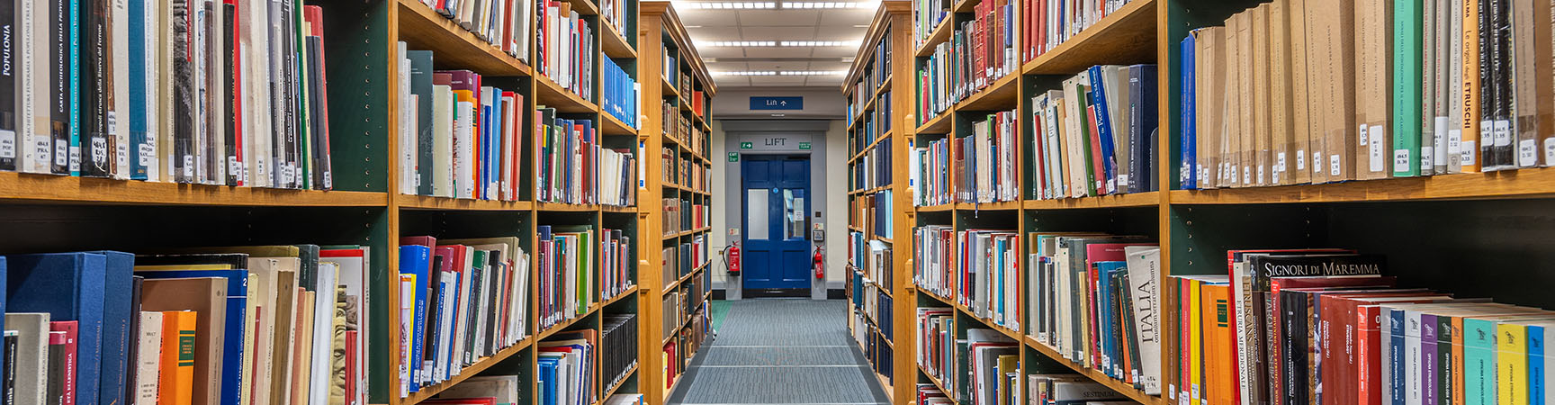 Two long rows of bookshelves either side of a corridor looking towards a blue door