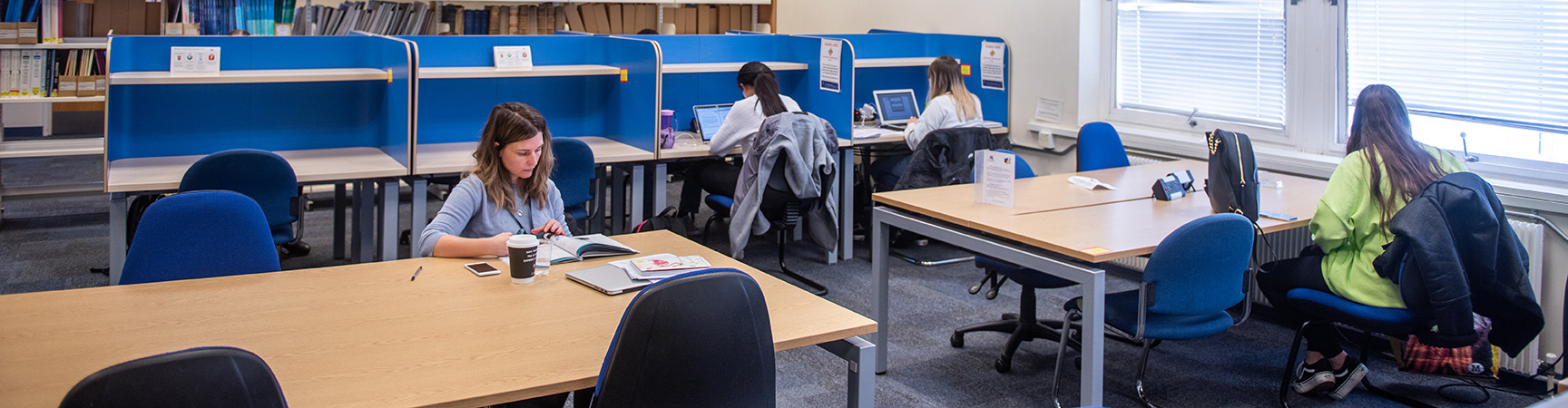 Tables in a room - some have blue separators - students are dotted about working at the desks