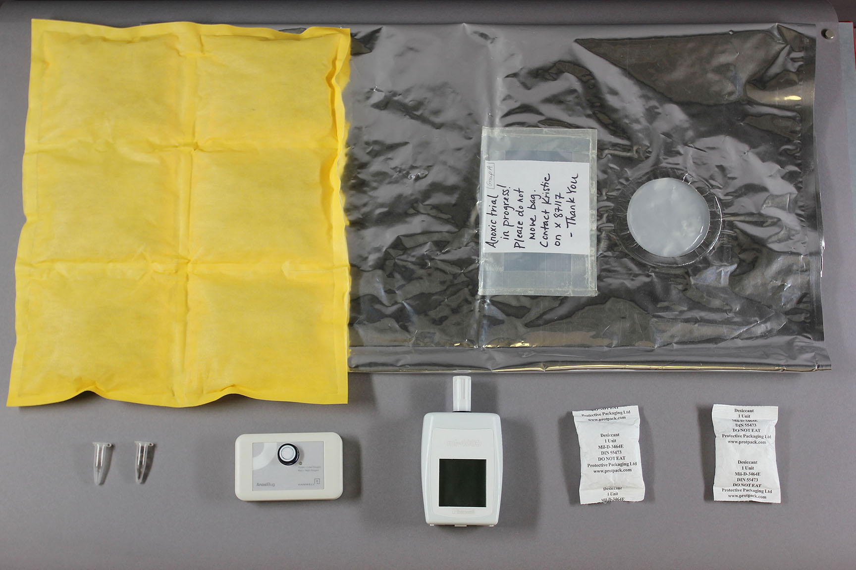 A photograph of three objects: a yellow cloth; a silver packet at a plastic wallet of 24 test swatches