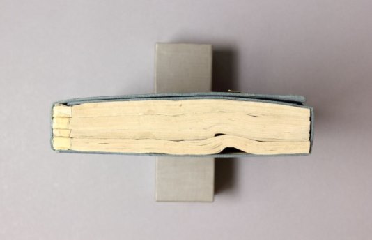 Bird's eye view of a bound manuscript - it is lying on its spine so the viewer can see the distortions in the pages