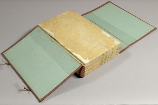 A large manuscript book with a hard cover - the cover is open on both sides and is light blue in colour