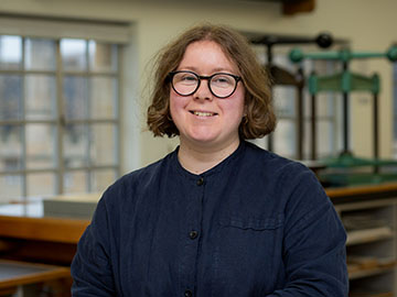 A woman with short blonde hair and glasses wearing a dark shirt