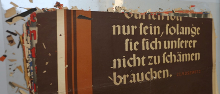 The top of a black poster - with German writing at the top - there are flakes and small paper fragments surrounding the main poster