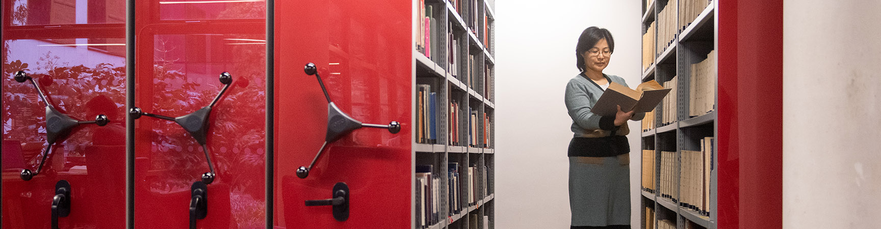 A librarian reading a book standing between two red bookshelves