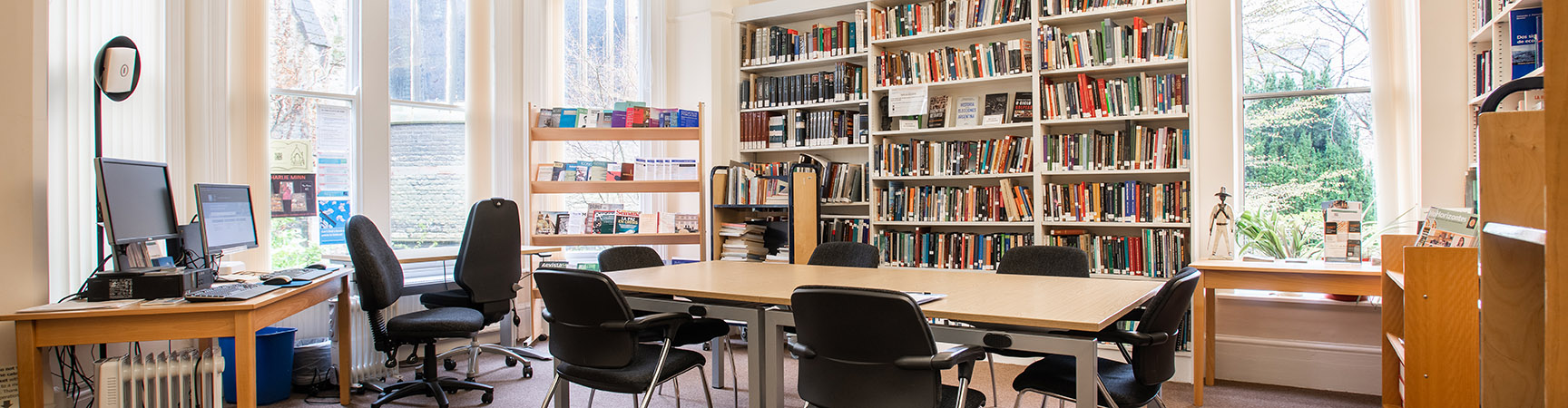 Six chairs around a long table with a bookshelf behind