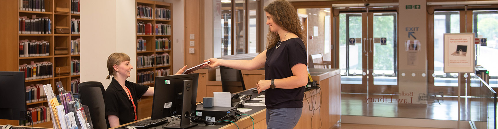 A librarian behind a desk hands over a book to a student