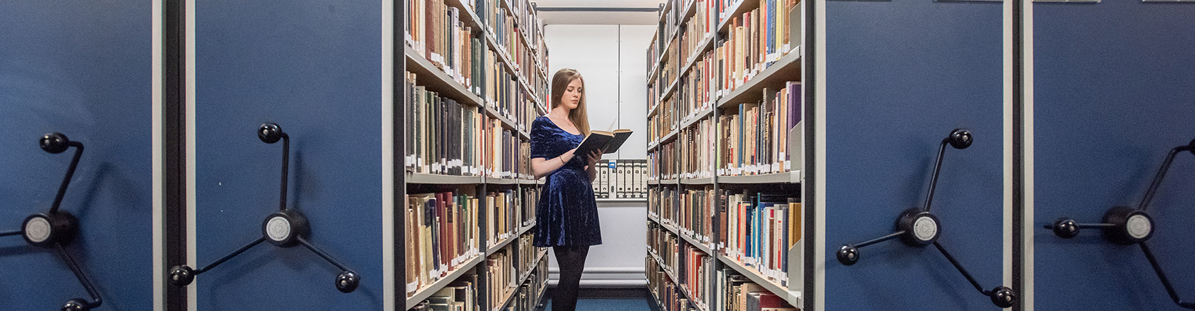 A student holding a book between two bookshelves