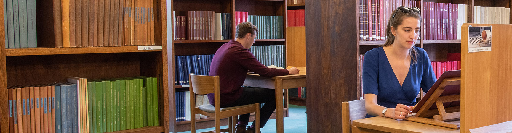 Two students working at two different desks surrounded by bookshelves