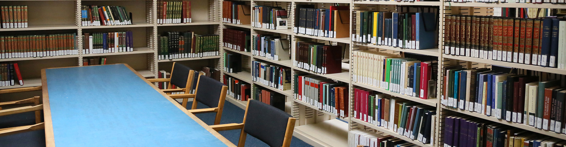 A long blue table surrounded by bookshelves