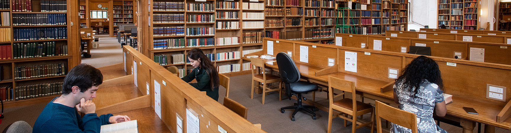 Four rows of wooden desks, each with wooden separators. Five students are dotted at the desks around the room.