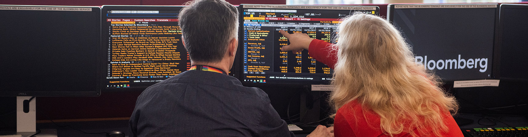 Two people sit in front of the computers showing Bloomberg detail