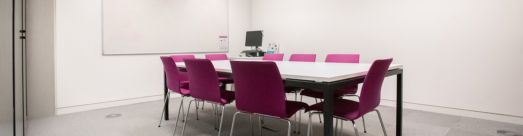 Nine purple chairs surrounding a white desk in a room