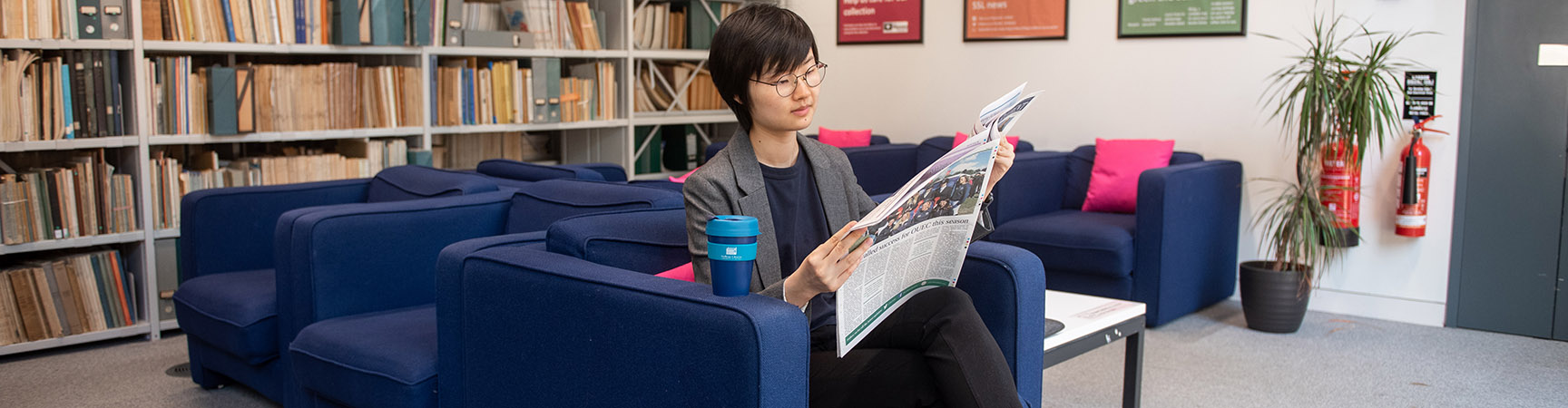 A woman reading a newspaper on a blue sofa