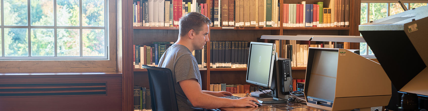 A student sitting at a desk in front of a microfiche reader