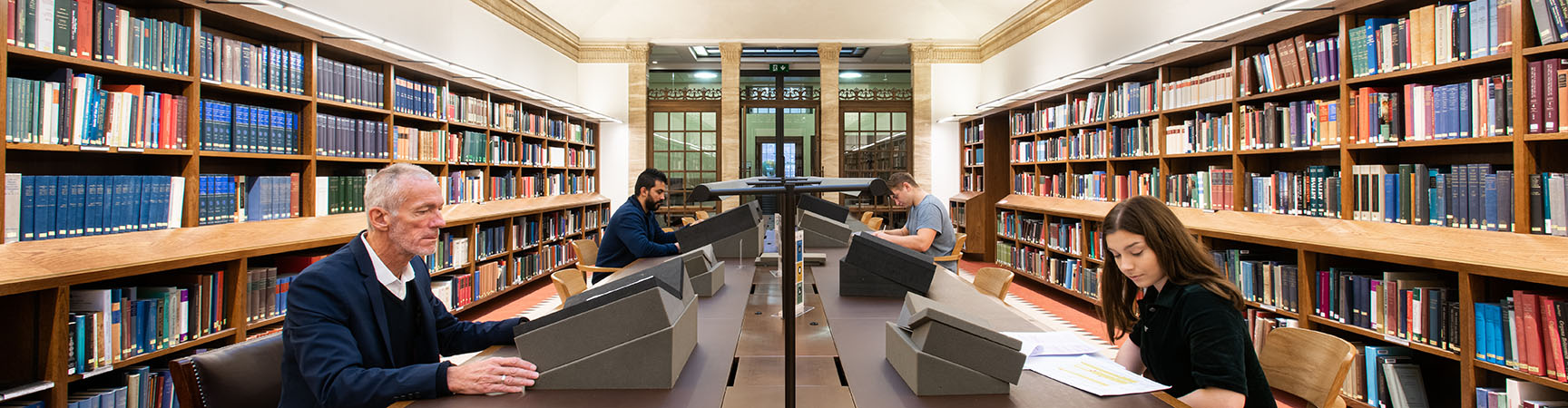 Two readers sit opposite each other each consulting special collections material - bookshelves run down the walls on either side of the room