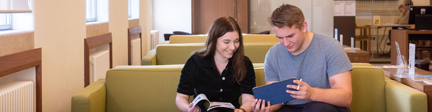 Two students looking at a book on a green sofa