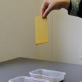 A piece of yellow paper with a red edge is removed from a tub of red dye