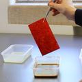 A piece of red paper is removed from a tub of dark red dye