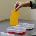 A piece of yellow paper with a red edge is removed from a tub of red dye