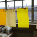 Four pieces of paper attached with paper clips to a line, dyed in shades of orange and yellow