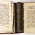 A medieval manuscript open there is writing on both pages and you can see the brown spine of the cover