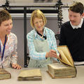 Three people stand next to each other - they are looking at a table where there are three large bound manuscripts