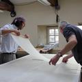 Two people stand either side of a table - they hold a sheet of white lining between them