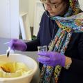 A woman wearing a colourful headscarf adds ash to a red substance in muslin