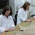 Two conservators stand and work on removing a beige lining from the back of the map