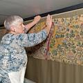 A woman reaches to the top of the tapestry map and holds it against its olive green background