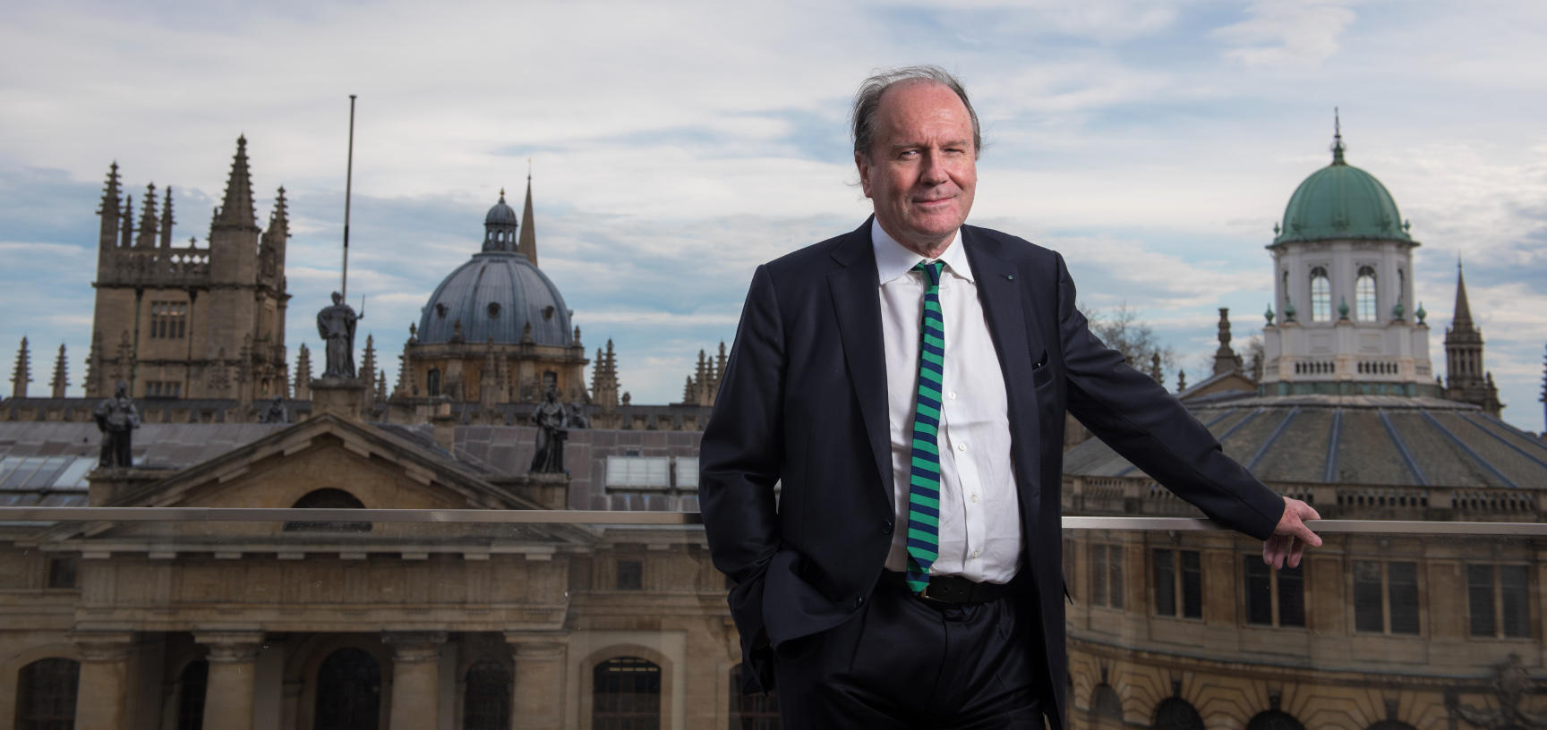 William Boyd stands on a balcony in front of the Oxford skyline