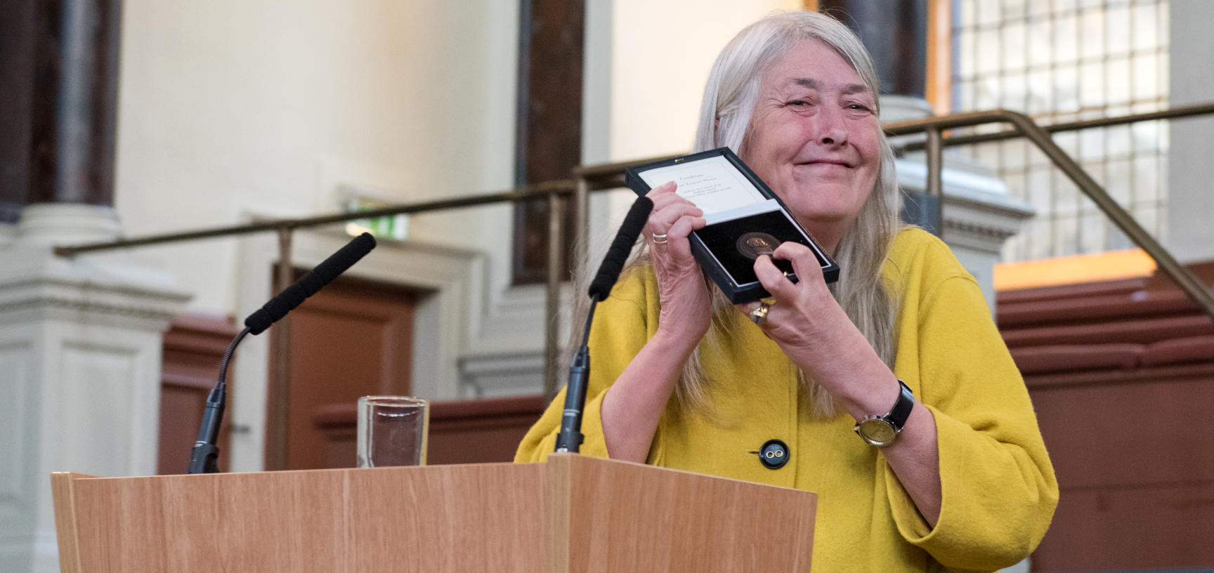 Professor Dame Mary Beard stands beside a speaker's podium holding the Bodley Medal