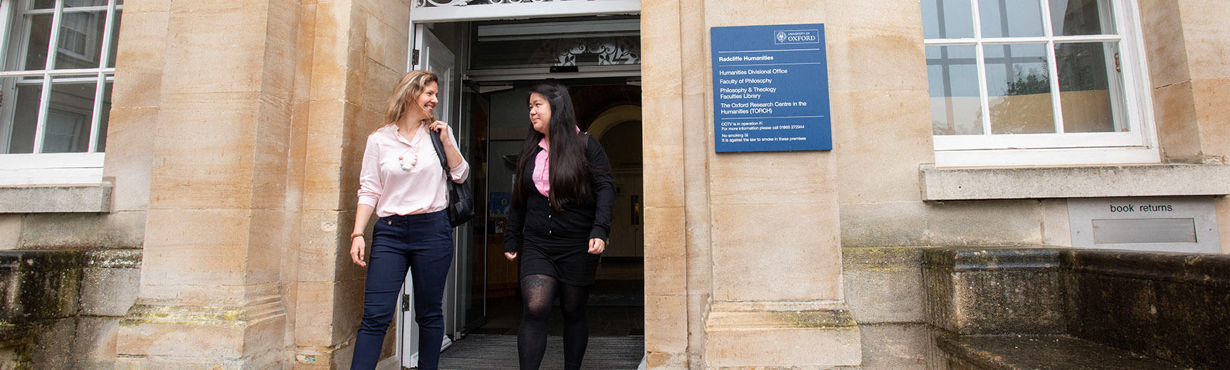 Two students leave a beige stone building