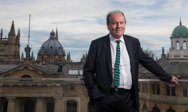 William Boyd stands on a balcony in front of the Oxford skyline