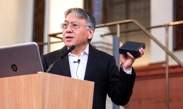 Sir Kazuo Ishiguro stands in front of a microphone and laptop, holding the Bodley Medal in its box