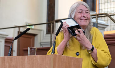 Professor Dame Mary Beard stands beside a speaker's podium holding the Bodley Medal