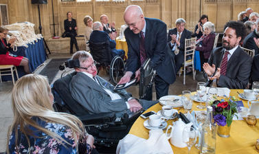 A man in a dark suit presents the Bodley Medal to Stephen Hawking, surrounded by people
