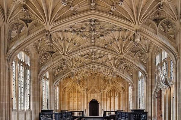 The inside of Divinity School - pale stone makes up the walls and ornately decorated ceiling, there are windows down each side and at the far end a small arched wooden door