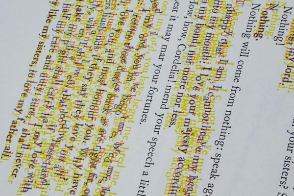 A slanted view of a page of printed type with some lines blurred and outlined in yellow