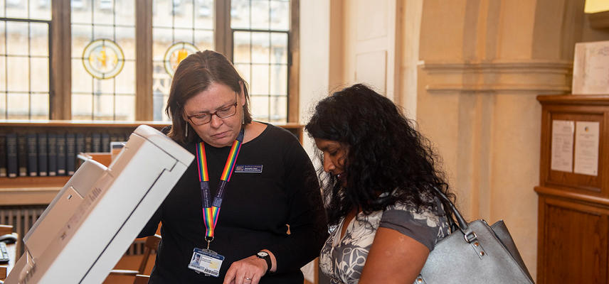 A member of library staff helps a library user to scan a book on a library scanner