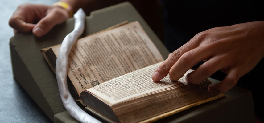 A hand points to a page of a book on a book rest