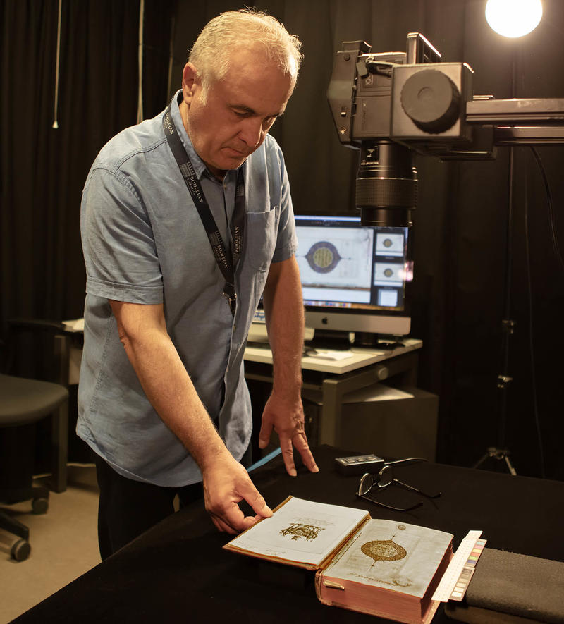Photographer Nick Cistone looks at an open rare book under a lamp