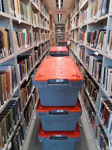 Six plastic boxes with red lids in between full bookshelves