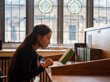 A woman looks at a book at a wooden desk