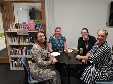 Four women around a table in a space with a bookshelf behind