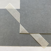 A corner of paper mounted on the edge of a grey piece of card, with a long rectangular paper strip under the grey