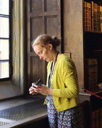 A woman stands in an old part of the library - the walls are panelled with wood - and she is looking at a piece of monitoring equipment in her hands