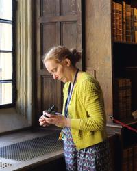 Catherine Harris A woman stands in an old part of the library - the walls are panelled with wood - and she is looking at a piece of monitoring equipment in her hands