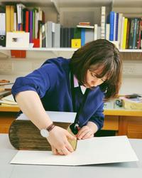 A woman leans over a large old book - she is wrapping it in a protective cover